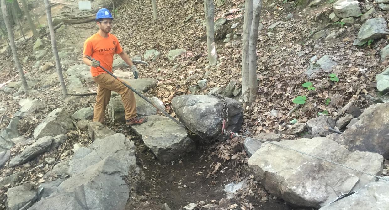 Crew member using a rock bar and a grip hoist to set a stepping stone.  